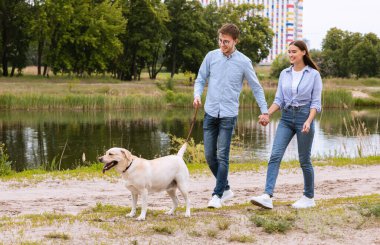 Köpeğiyle yürüyen mutlu genç bir çiftin portresi.