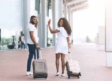 Mutlu afro çift havaalanı girişine yürüyor ve kameraya el sallıyor.