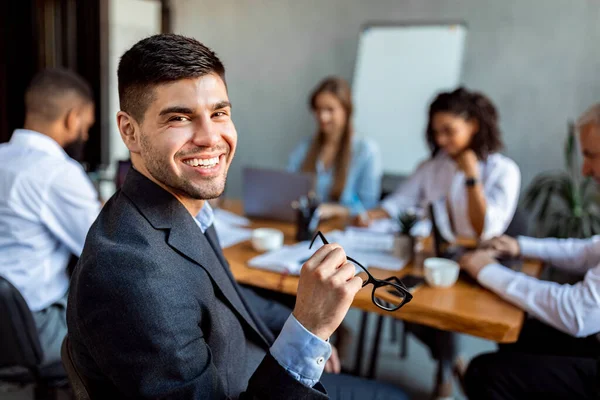 Jovem empresário sorrindo sentado com equipe de negócios no escritório moderno — Fotografia de Stock