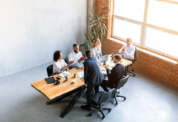 Colleagues Handshaking During Corporate Meeting Sitting At Desk In Office