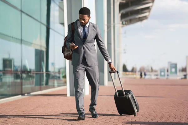 Empresario africano usando teléfono caminando con maleta de viaje en el aeropuerto — Foto de Stock