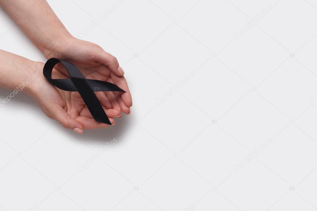 Black awareness ribbon in hands on white background
