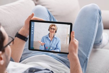 Online danışmanlık. Kanepedeki adam yetişkin bir kadının tabletine bakar ve onunla iletişim kurar.