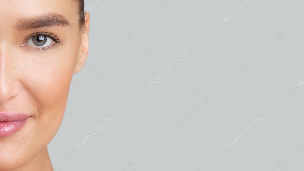 Half-face portrait of young beautiful woman with perfect skin, closeup, empty space for logo or text on gray wall, banner