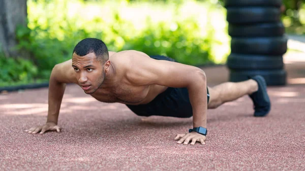Shirtloser muskulöser Schwarzer, der Liegestütze auf der Joggingstrecke im Stadtpark macht — Stockfoto