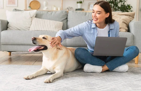 Ung kvinna hemma med laptop och glad hund — Stockfoto