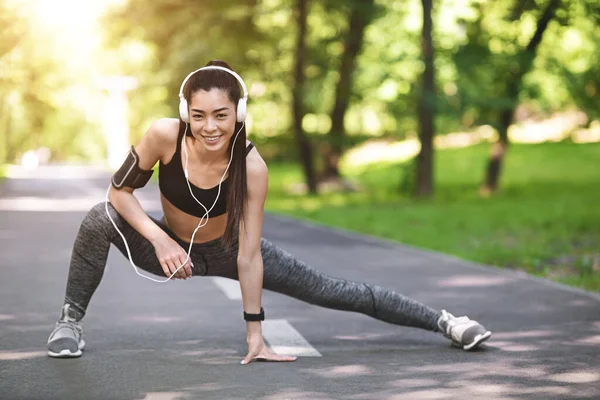 Deportiva asiática mujer en auriculares calentando antes de correr en parque — Foto de Stock