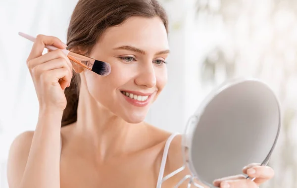 Smiling woman applying blush on face with brush tool — Stock Photo, Image