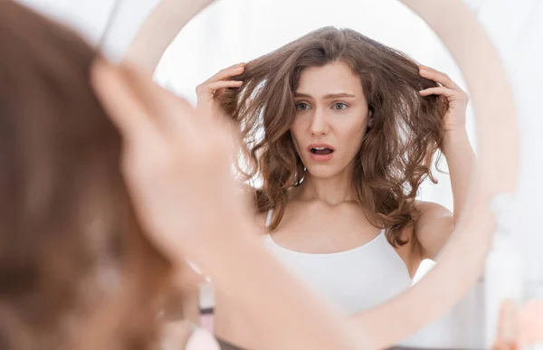 Šokovaná mladá žena drží vlasy, dívá se do zrcadla — Stock fotografie