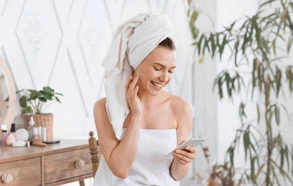 Chica feliz comprobando en las redes sociales mientras se aplica crema —  Fotos de Stock