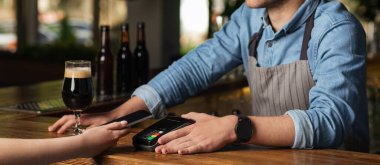 Barmen faturayı terminalle ödemeyi teklif ediyor, kız telefonu barın içinde tutuyor.