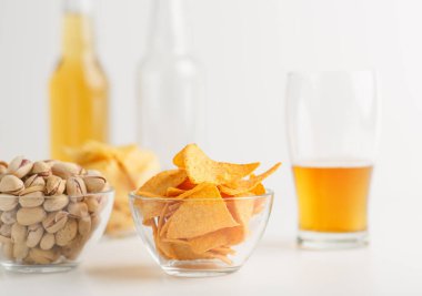Lezzetli atıştırmalıklar. Şam fıstığı ve cam kaselerde nachos, bardakta parlak bira, boş şişe ve dolu şişe.