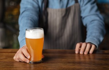 Yarım litre bira. Önlüklü ve mavi gömlekli barmen ahşap masa bardağı bira koydu.
