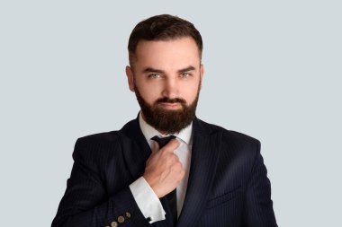 Takım elbiseli yakışıklı beyefendi kravatını gri arka plana göre ayarlıyor.