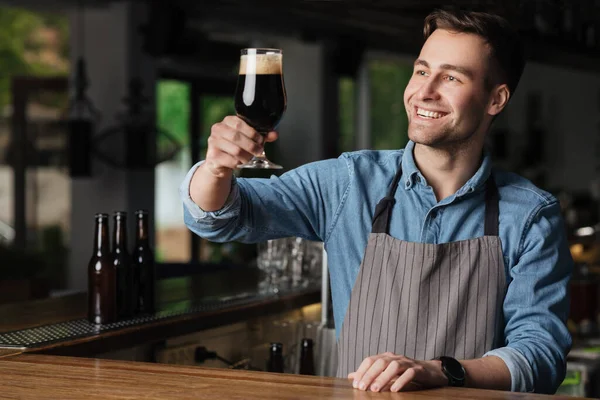 Birinci sınıf. Gülümseyen barmen elinde koyu biranın tadını çıkarıyor. — Stok fotoğraf