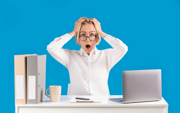 Starší sekretářka drží hlavu v šoku na svém pracovišti s notebookem, modré pozadí — Stock fotografie