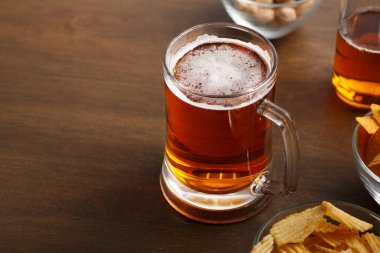 Kutlama için parlak bira bardağı. Kahverengi ahşap masada bira ve cips var.