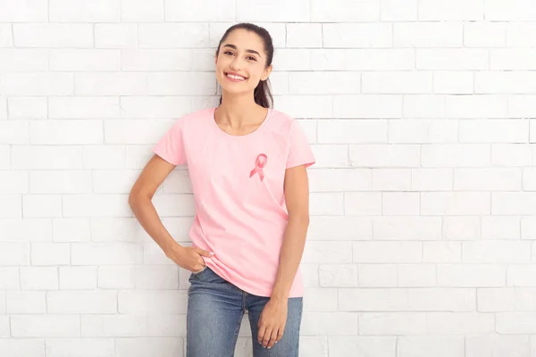핑크 리본 티 셔츠를 입은 젊은 여인 이 백 벽에 맞서서 있다 — 스톡 사진