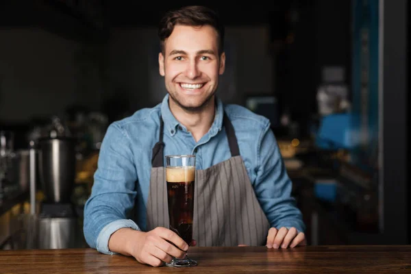 Pub de cerveja artesanal. Sorrindo cara coloca em vidro balcão de madeira bar de cerveja escura — Fotografia de Stock