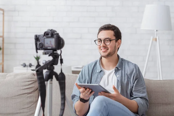 Video blogger en el lugar de trabajo en casa. Sonriente joven en gafas con tableta habla a la cámara — Foto de Stock