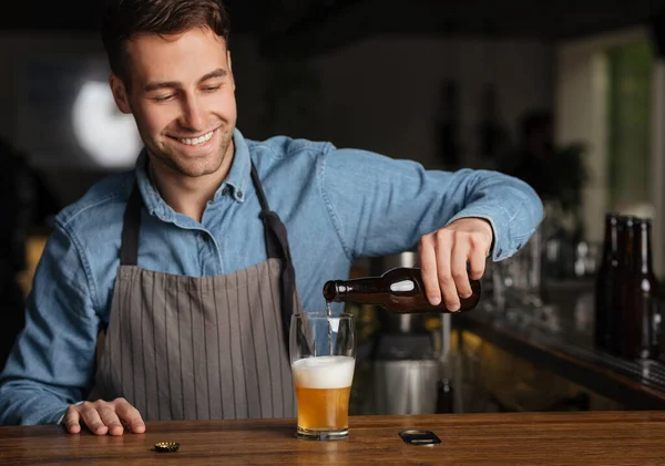 Barman verse de la bière dans une bouteille en verre, debout derrière le comptoir du bar à l'intérieur — Photo