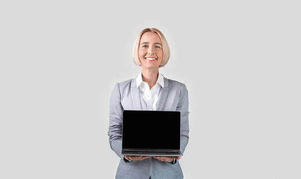 Happy businesswoman holding laptop computer with blank screen on light background, space for your design — Stock fotografie