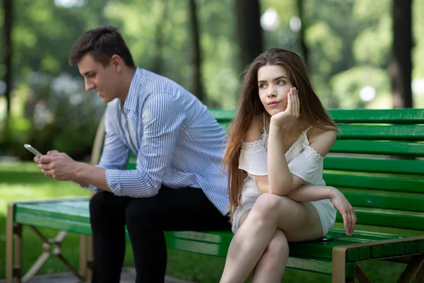 Vício em gadgets. Jovem entediada e seu namorado preso no celular em data maçante no parque — Fotografia de Stock