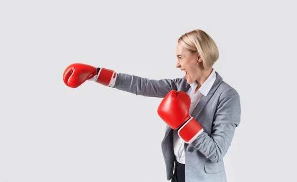 Angry businesswoman in boxing gloves making strike on light background — Stock Photo, Image