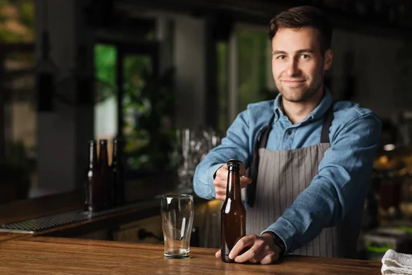 Ambachtelijk bier voor de klant. Barman opent fles bier, in de buurt van leeg glas — Stockfoto