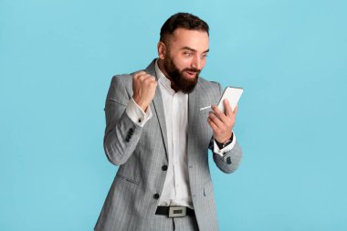 Akıllı telefona bakıp mavi arka planda EVET hareketi yapan heyecanlı genç iş adamı