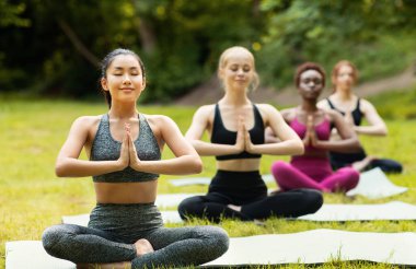 Çok uluslu kızlar açık hava yoga dersleri sırasında nefes egzersizleri ya da meditasyon yapıyorlar.