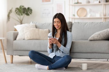 Gülümseyen Koreli kız evde yerde dinlenirken akıllı telefondan mesaj atıyor.