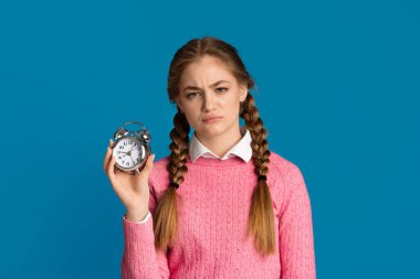 Oversleep concept. Tired teenager girl with pigtails holds alarm clock in her hands clipart