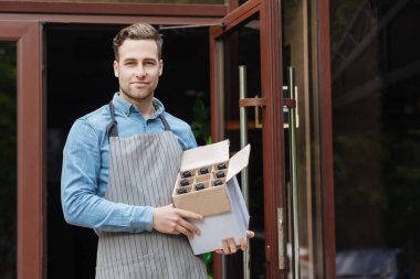 Önlüklü barmen barın girişinde şişelerle dolu bir kutu tutuyor.