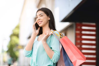 Alışveriş yaptıktan sonra cep telefonuyla konuşan Asyalı genç bir kadın.