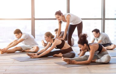 Yoga eğitmeni, grup dersi sırasında esneme egzersizleri yapan genç bir kadına yardım ediyor.