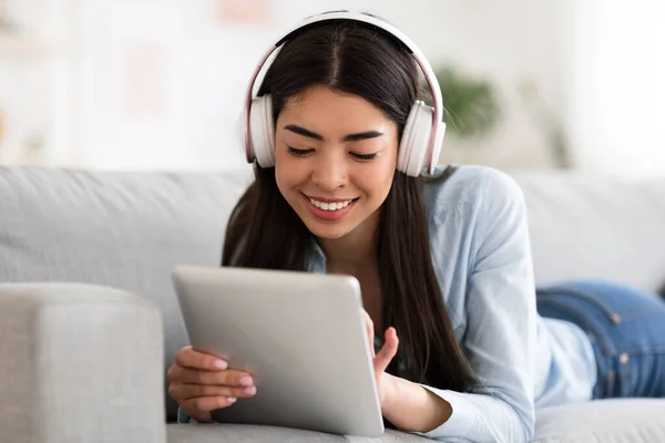 Home Pastime. Asian Girl Using Digital Tablet And Listening Music In Headphones