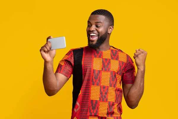 Feliz hombre negro sosteniendo el teléfono y expresando felicidad — Foto de Stock