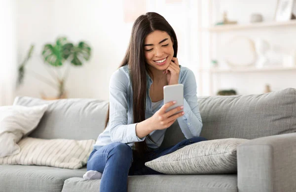 Joven chica asiática mensajería en el teléfono inteligente mientras se relaja en el sofá en casa — Foto de Stock