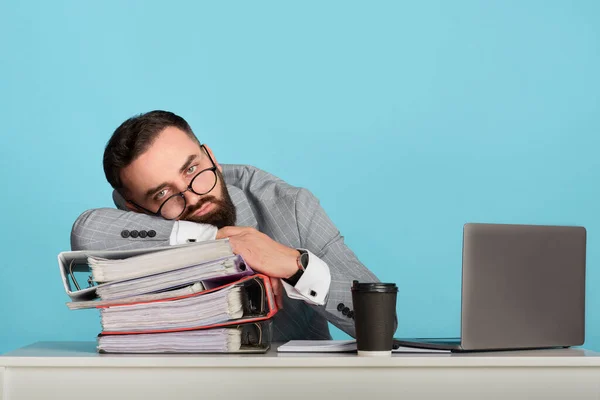 Přepracovaný podnikatel ležící na stole poblíž notebooku na modrém pozadí, prázdné místo — Stock fotografie
