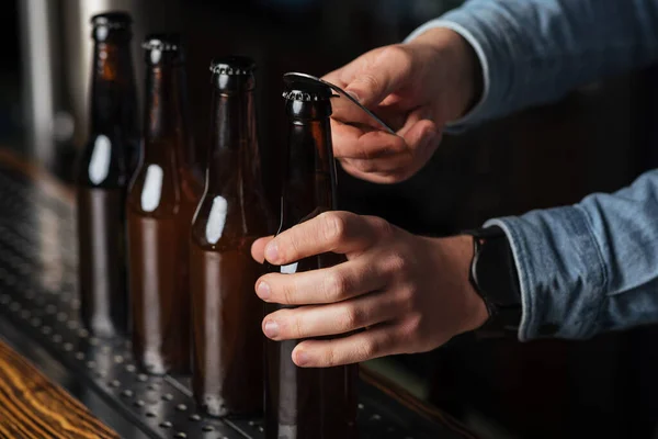Biercompetitie. Barman met klok, opent flesjes bier op houten bar teller — Stockfoto