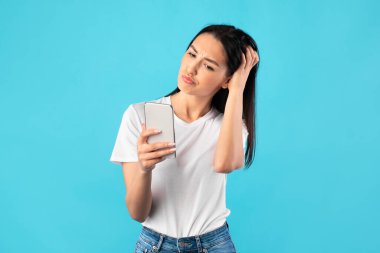 Kafası karışmış genç bir kadın cep telefonu kullanıyor.