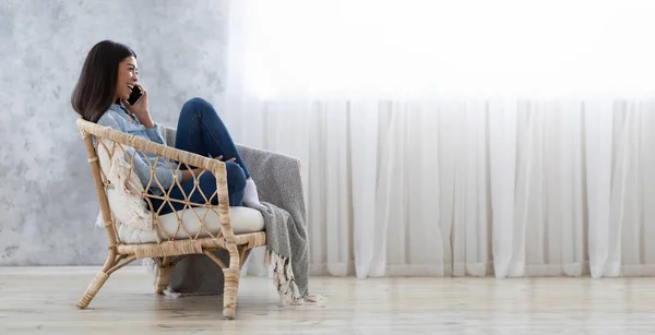 Una llamada agradable. Querida mujer asiática hablando por celular mientras descansa en sillón —  Fotos de Stock