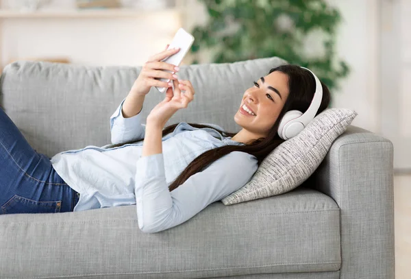 Chica asiática disfrutando escuchando música en el teléfono inteligente con auriculares inalámbricos en casa — Foto de Stock