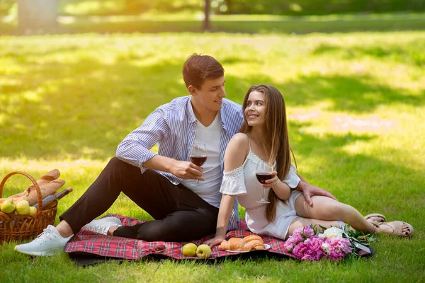 Casal jovem afetuoso celebrando aniversário com vinho em piquenique no parque — Fotografia de Stock