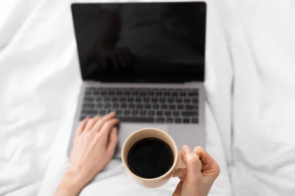 Женщина пьет кофе и работает в сети на ноутбуке, пове — стоковое фото