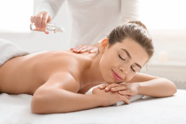 Massagem terapeuta derramando óleo na jovem mulher de volta — Fotografia de Stock