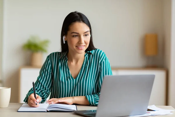 Mujer en el ordenador portátil tomando notas de aprendizaje con auriculares en la oficina — Foto de Stock