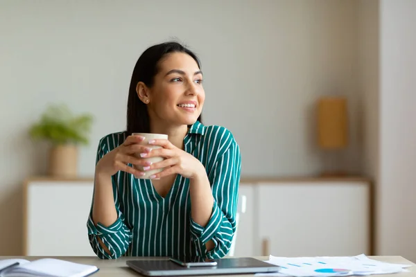 Mujer emprendedora sonriendo tomando café en el lugar de trabajo sentado en la oficina —  Fotos de Stock