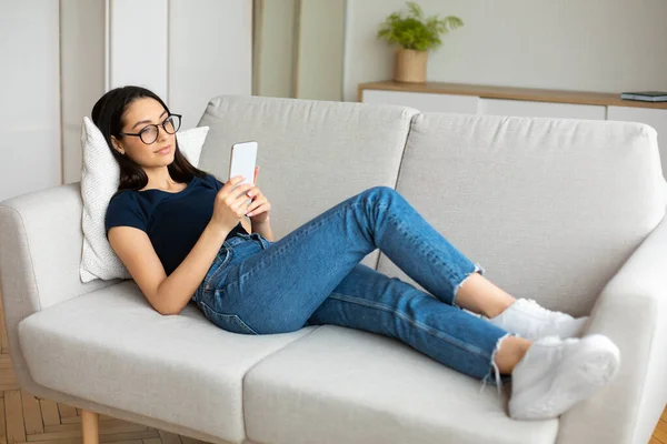 Relaxált lány telefonos SMS-ezés Online hazugság kanapén beltéri — Stock Fotó